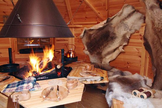 Innenraum einer Grillkota von Finnhaus Wolff mit Feuer in der Mitte, Essensgedeck aus Holz und Tierfellen an der Wand.