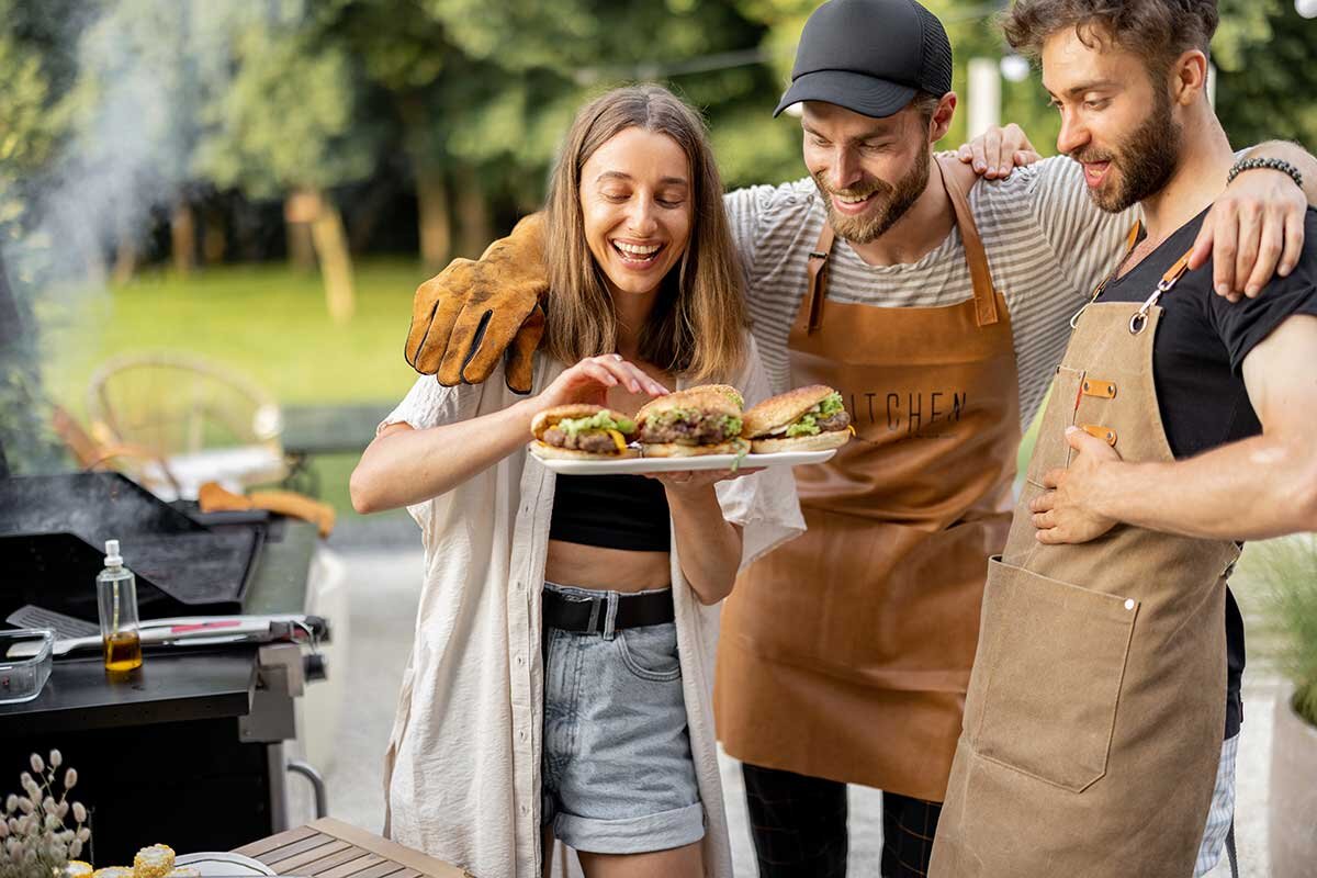 2 Männer und eine Frau stehen neben Grill mit Teller voller Burger.